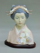 A Lladro porcelain bust of a geisha on a wooden stand. 25.5 cm high overall.