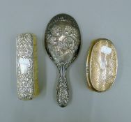 A silver hand mirror and two silver backed brushes. The former 25.5 cm long.