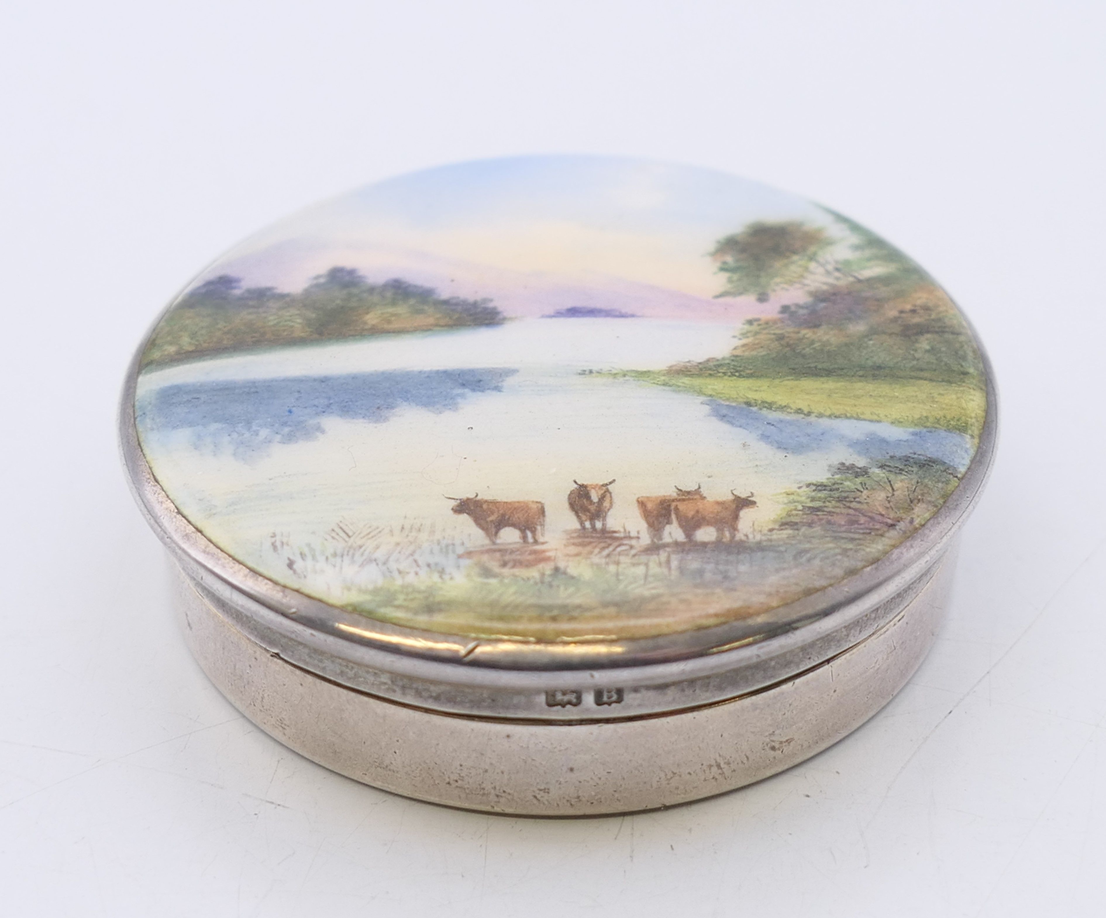 A silver and enamel pill box decorated with cattle in a mountainous landscape,