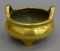 A Chinese gilt bronze tripod censer of compressed form with twin upright handles,