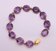 An antique gilt metal collet set amethyst coloured paste riviere bracelet. 15 cm long.