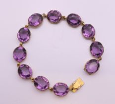 An antique gilt metal collet set amethyst coloured paste riviere bracelet. 15 cm long.