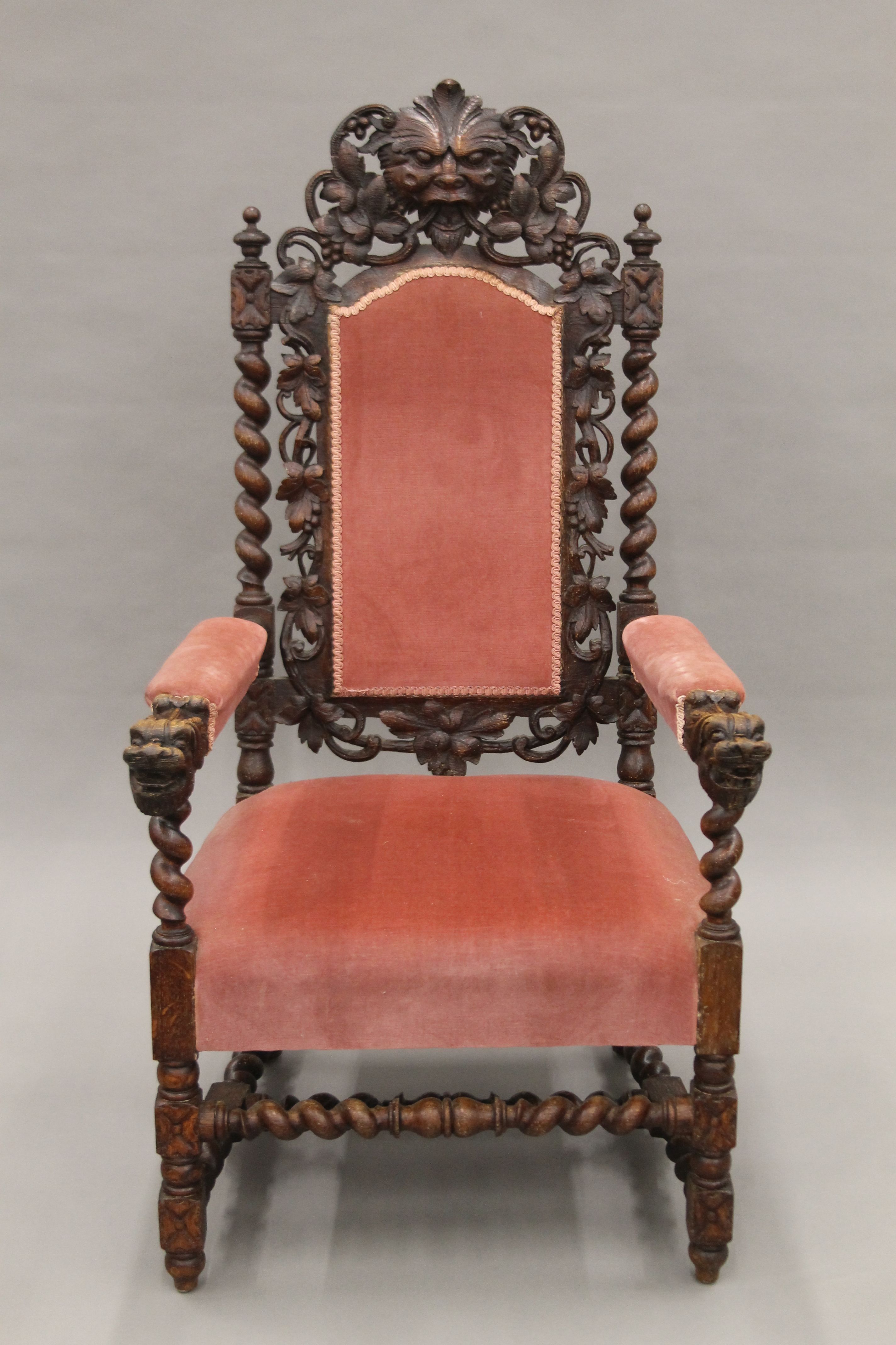 A 19th century carved oak upholstered open armchair with greenman back and dolphin form arms.