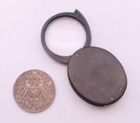 A 1902 German silver Funf mark and a bakelite magnifying glass by Philip Harris Ltd, Birmingham.