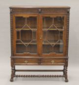 An early 20th century carved oak two door glazed barley twist cabinet.