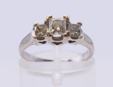 A 14 k white gold three-stone emerald-cut diamond ring. Ring size L.
