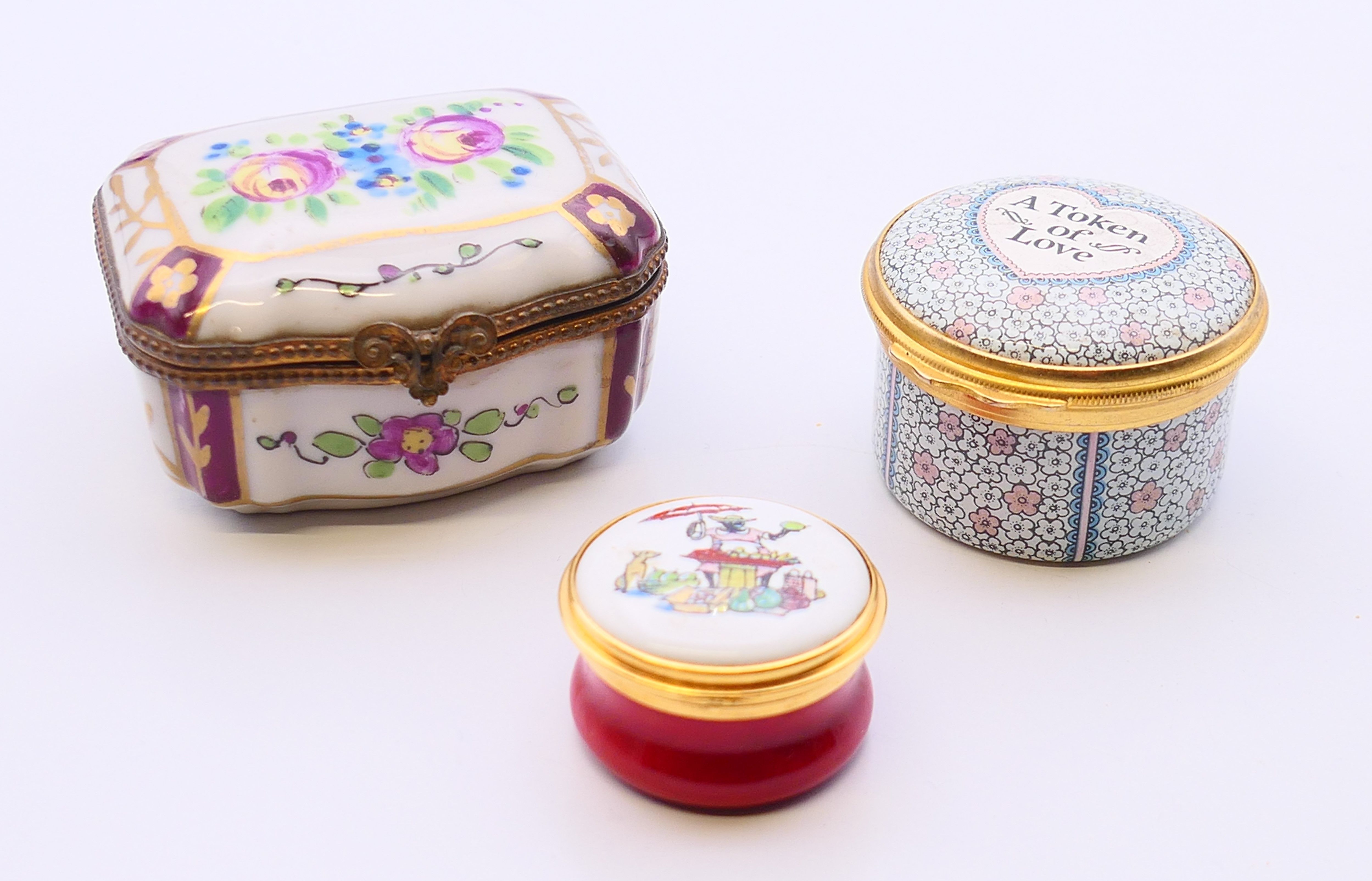 Three small decorative pill boxes, one porcelain, two enamel. The largest 6 cm x 5 cm.