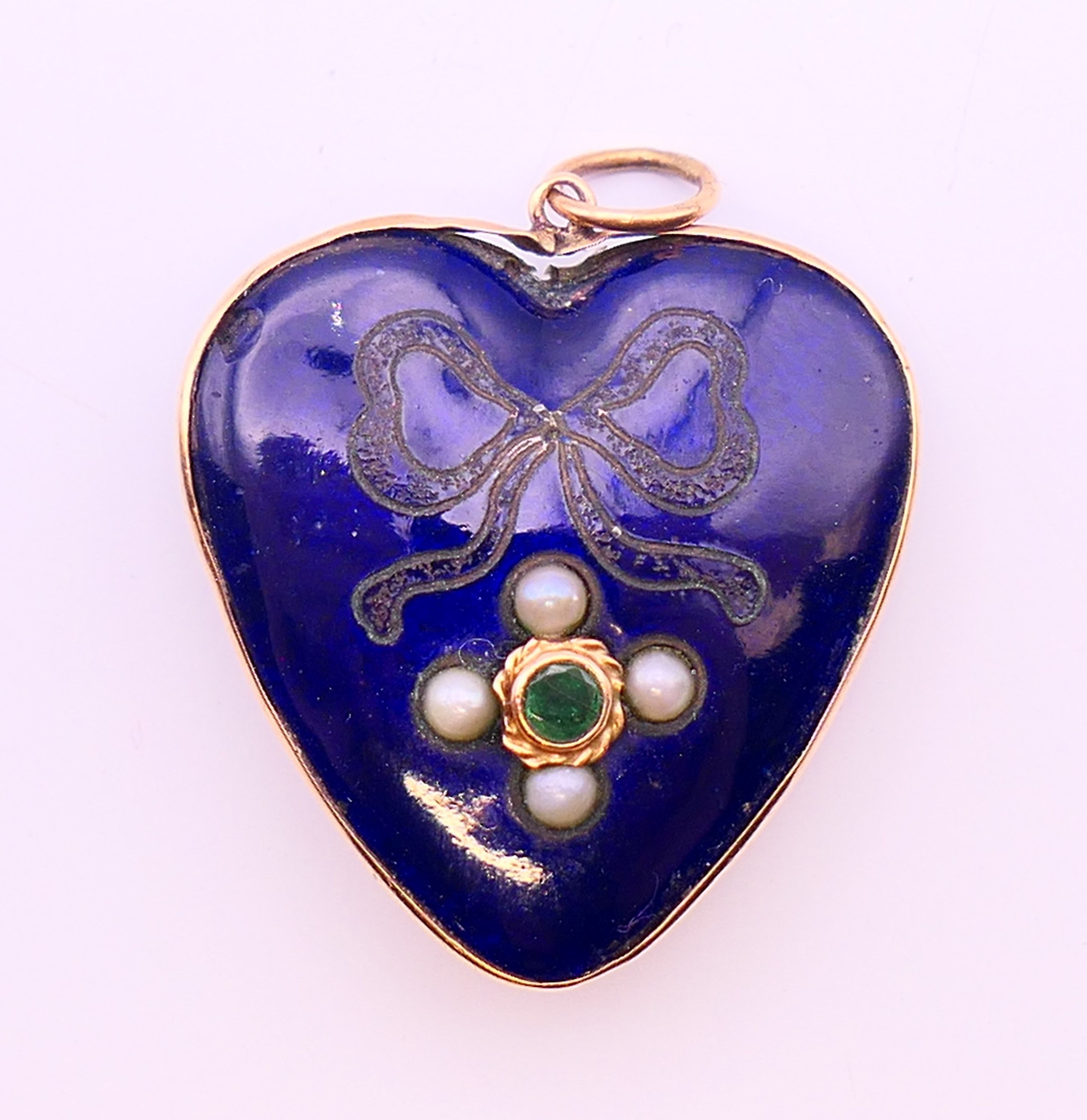 An enamel heart shaped pendant locket set with seed pearls and an emerald. 2.5 cm high.