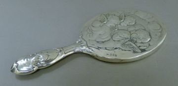 A silver hand mirror decorated with cherubs. 28.5 cm high.