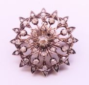 An unmarked diamond set pierced flower-form brooch/pendant. 3.5 cm diameter. 14.