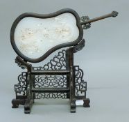 A white jade screen on a carved wooden stand. 31 cm high.
