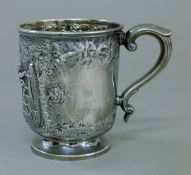 A silver Christening mug embossed with children playing on a gate. 9 cm high. 6.3 troy ounces.