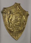 A 19th century brass shield repousse decorated with various sporting motifs, including cycling,