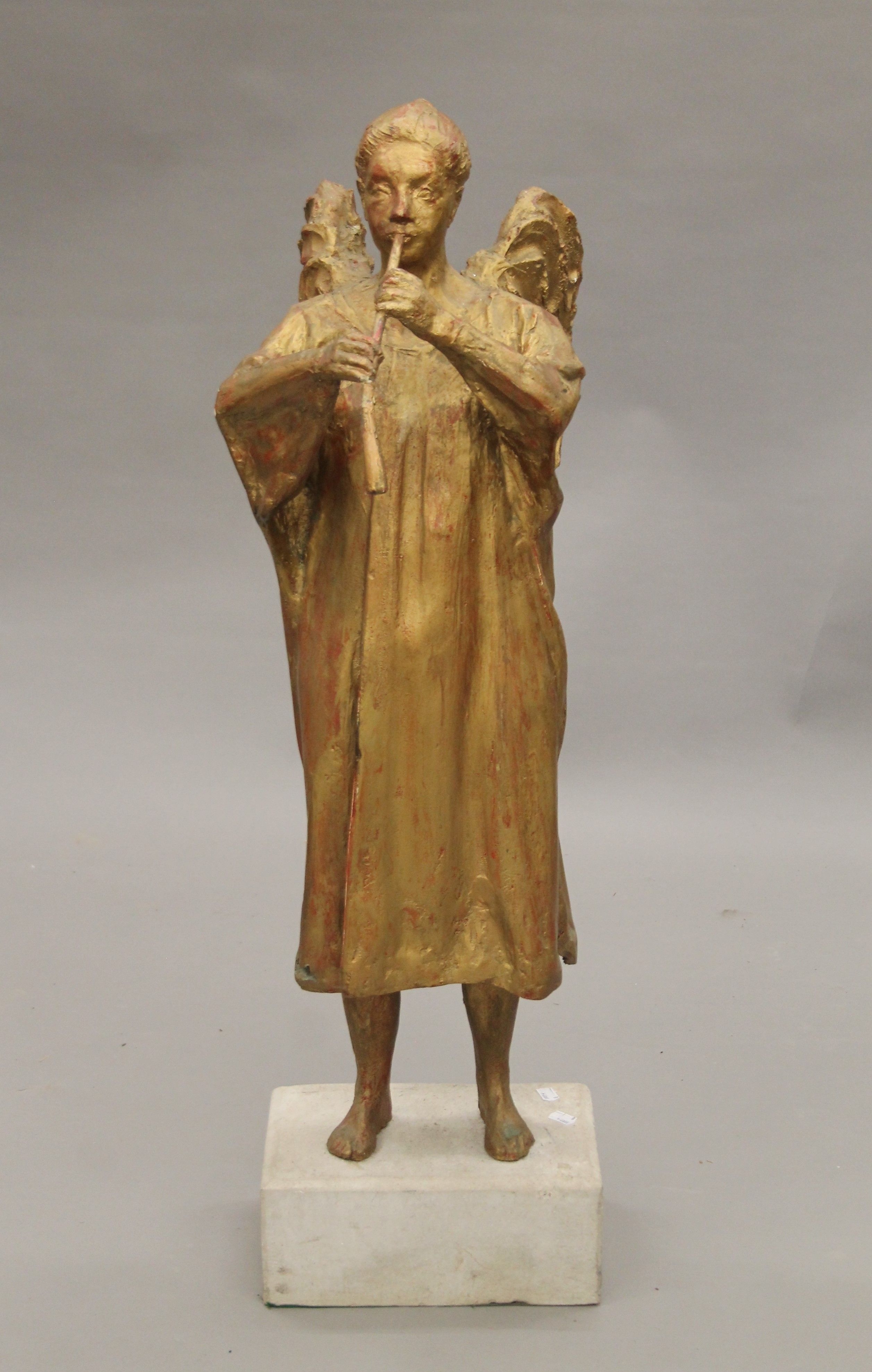 A gilt-painted sculpture of an angel mounted on a composite stone plinth base. 105 cm high.