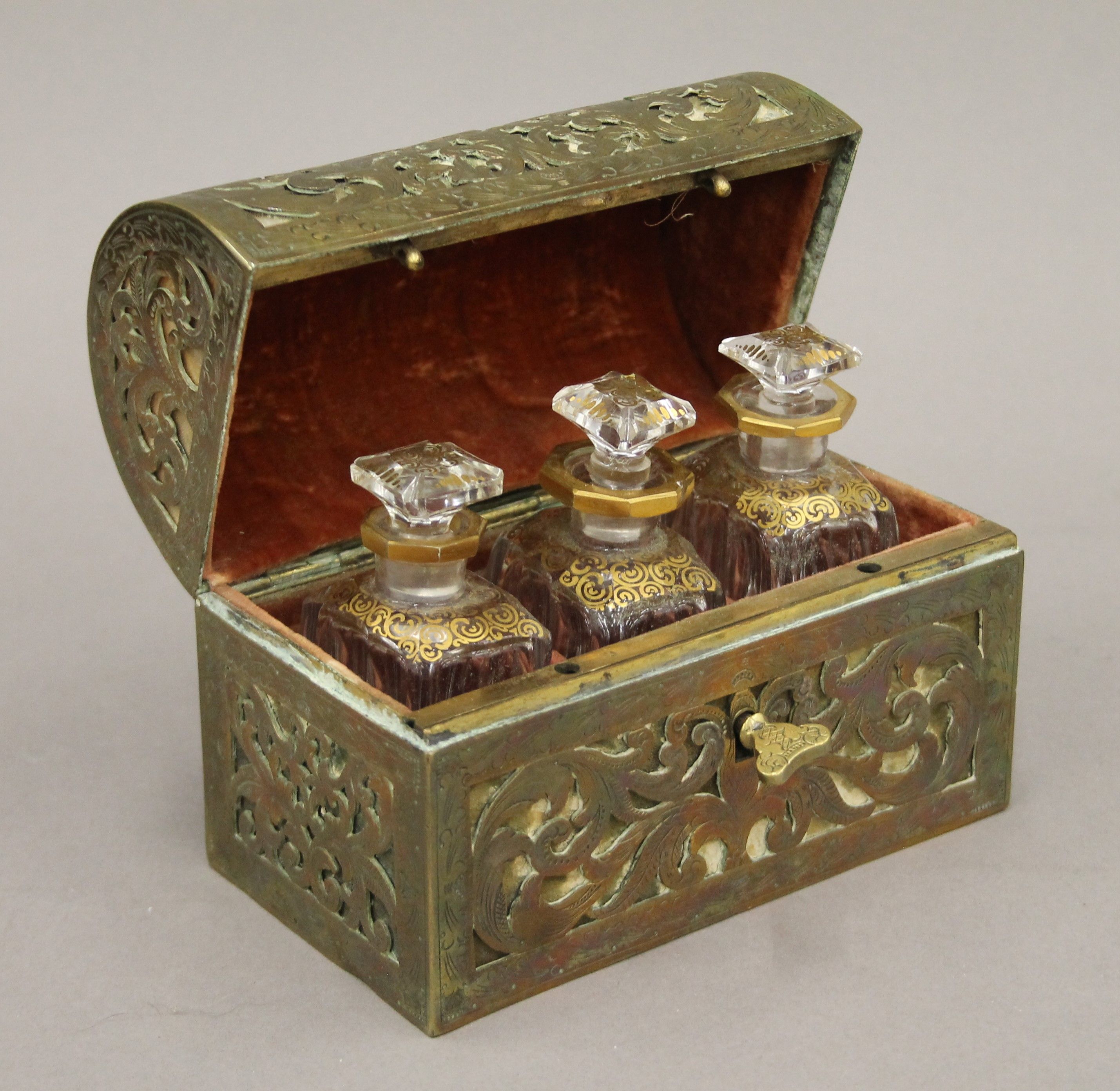 An antique dome-shaped pierced brass velvet-lined perfume casket containing three gilded cut glass