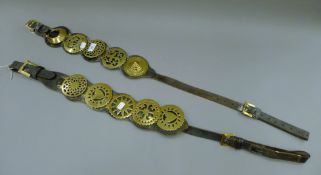 Two leather straps of horse brasses. 64 cms long.