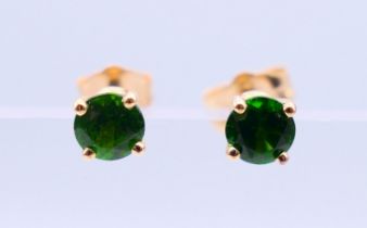 A pair of 14 k gold earrings set with green gemstones, possibly emeralds. 0.5 cm diameter.