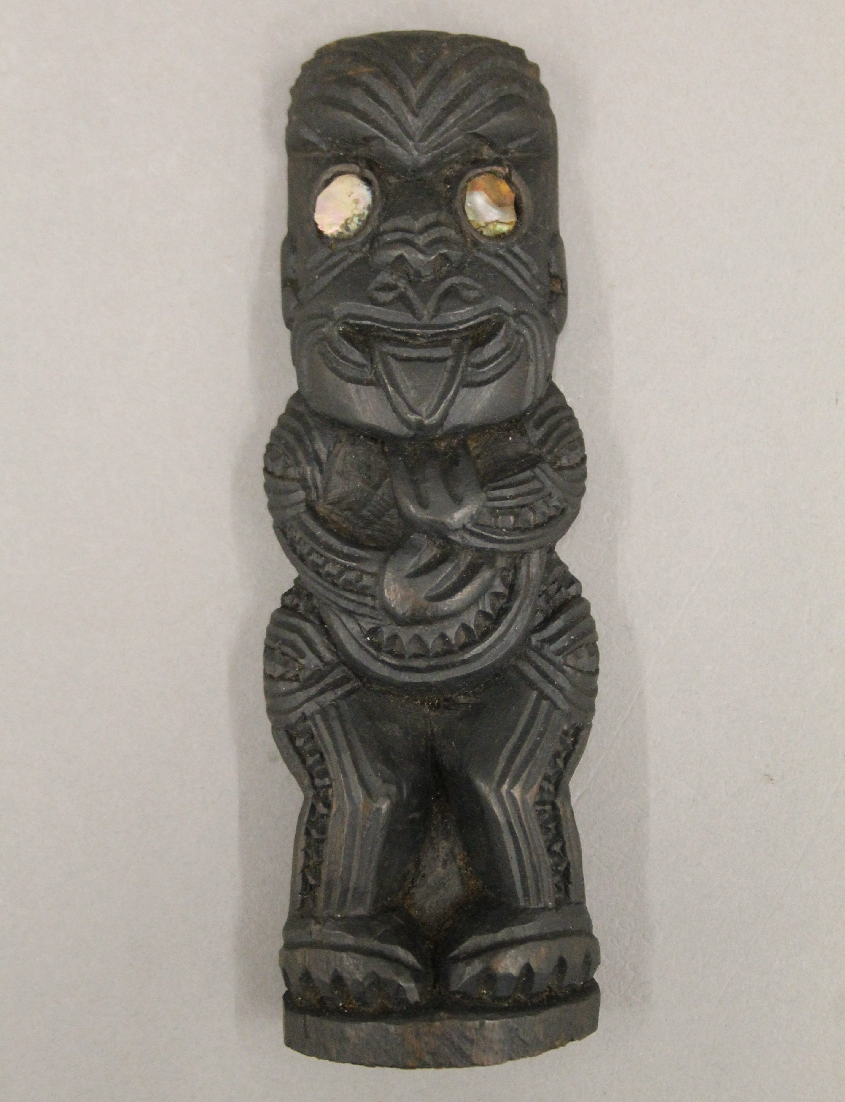 A carved wooden Maori Tiki with inset abalone shell eyes. 16 cm high.