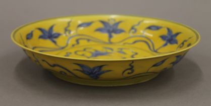 A Chinese yellow ground porcelain dish decorated with blue trailing foliage. 20.5 cm diameter.