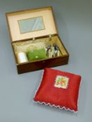 A quantity of lace-making bobbins in a box with two cushions and a large red pin cushion.