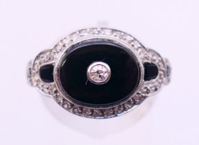 A platinum, black onyx and diamond ring. Ring size N/O.