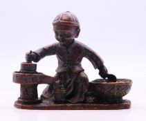 A bronze of a boy between two cooking vessels. 6 cm high.