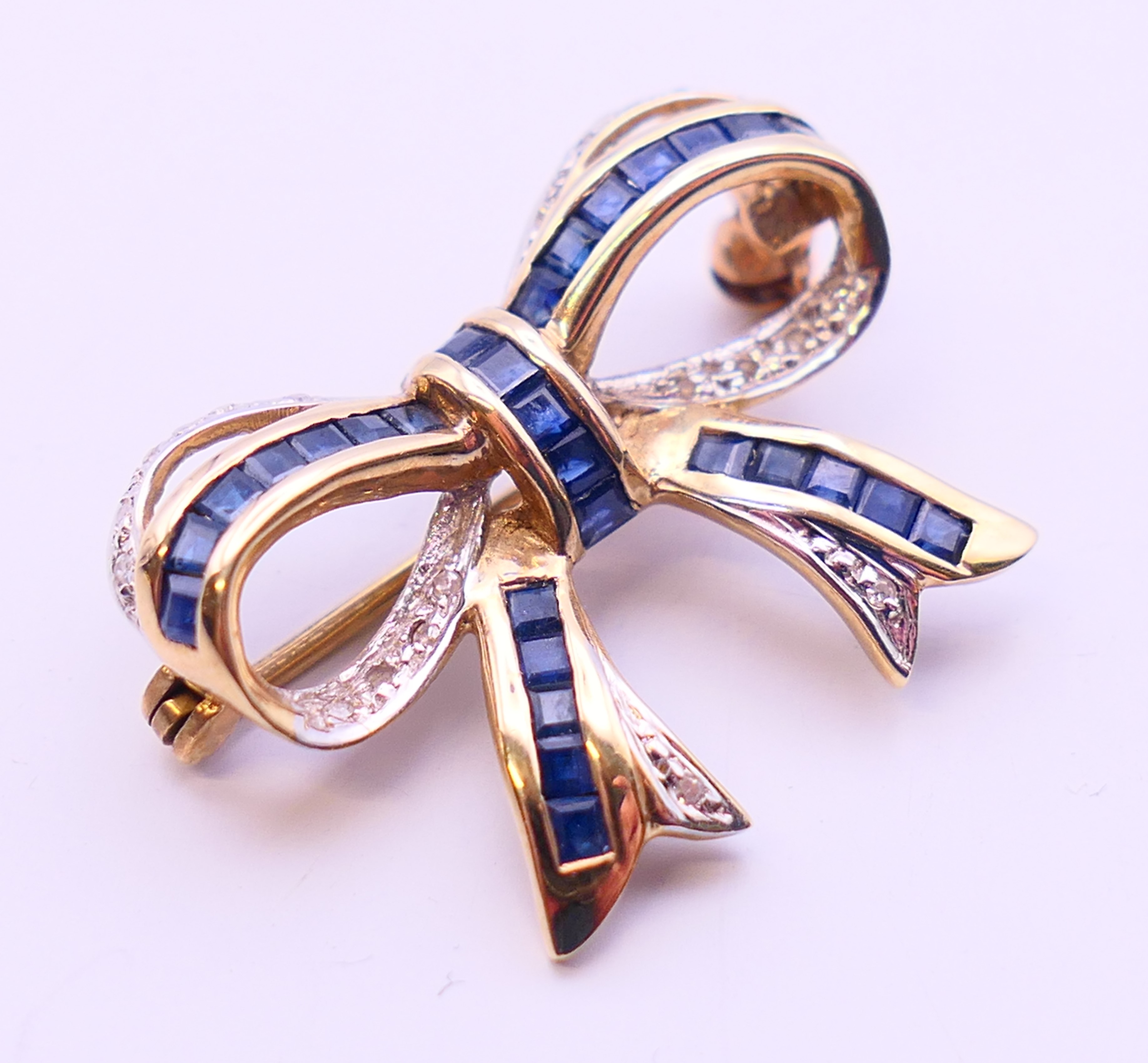 A 9 ct gold bow brooch set with mid-blue baguette sapphires and diamonds. 2.5 cm x 2 cm. 3. - Image 2 of 3