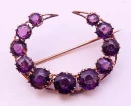 An eleven stone amethyst crescent brooch, circular amethysts 3.5-5.7mm, stamped 333. 3 cm x 2.5 cm.