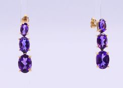 A pair of 10 K gold and amethyst three stone drop earrings. 2 cm high.