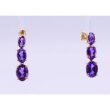 A pair of 10 K gold and amethyst three stone drop earrings. 2 cm high.