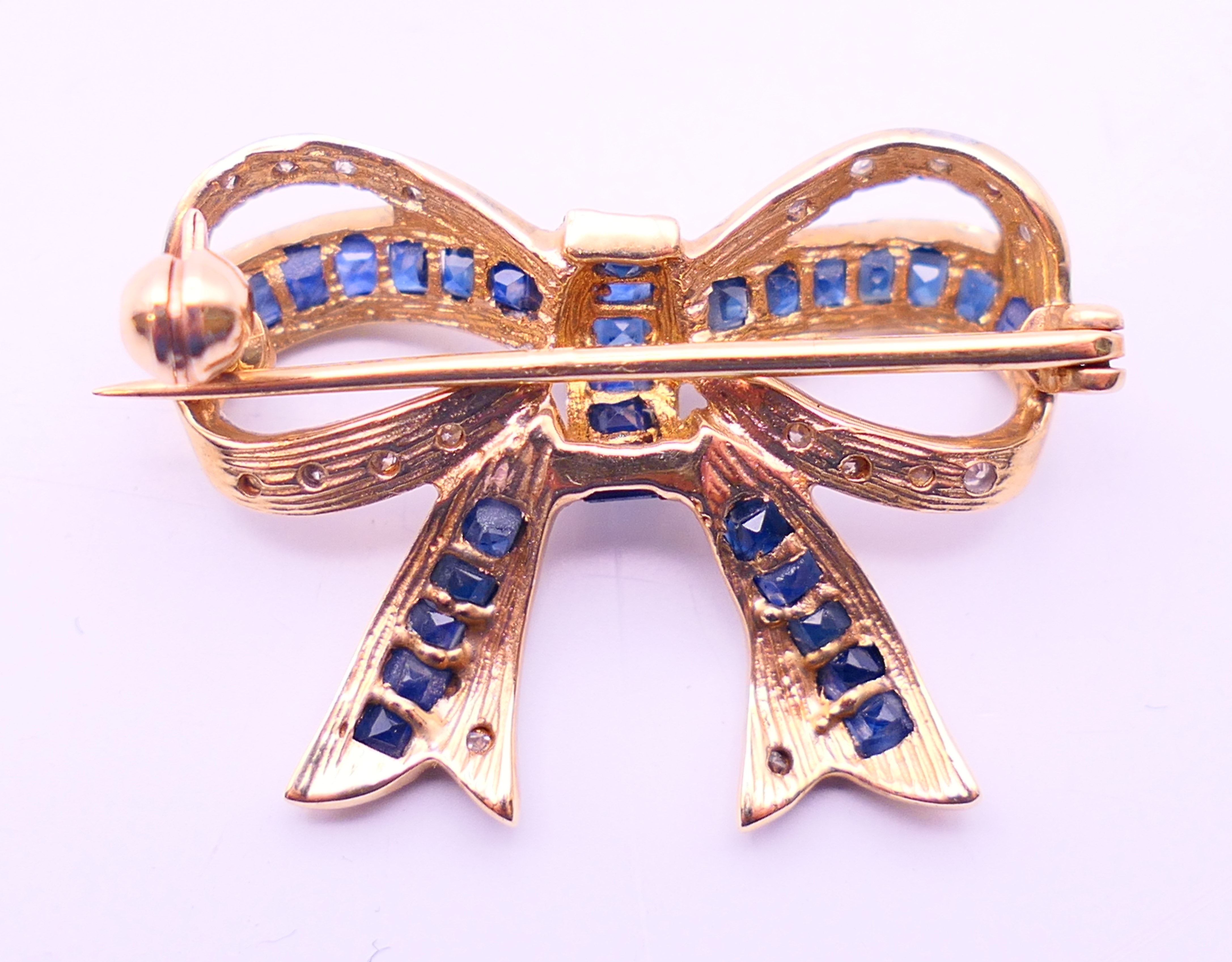 A 9 ct gold bow brooch set with mid-blue baguette sapphires and diamonds. 2.5 cm x 2 cm. 3. - Image 3 of 3