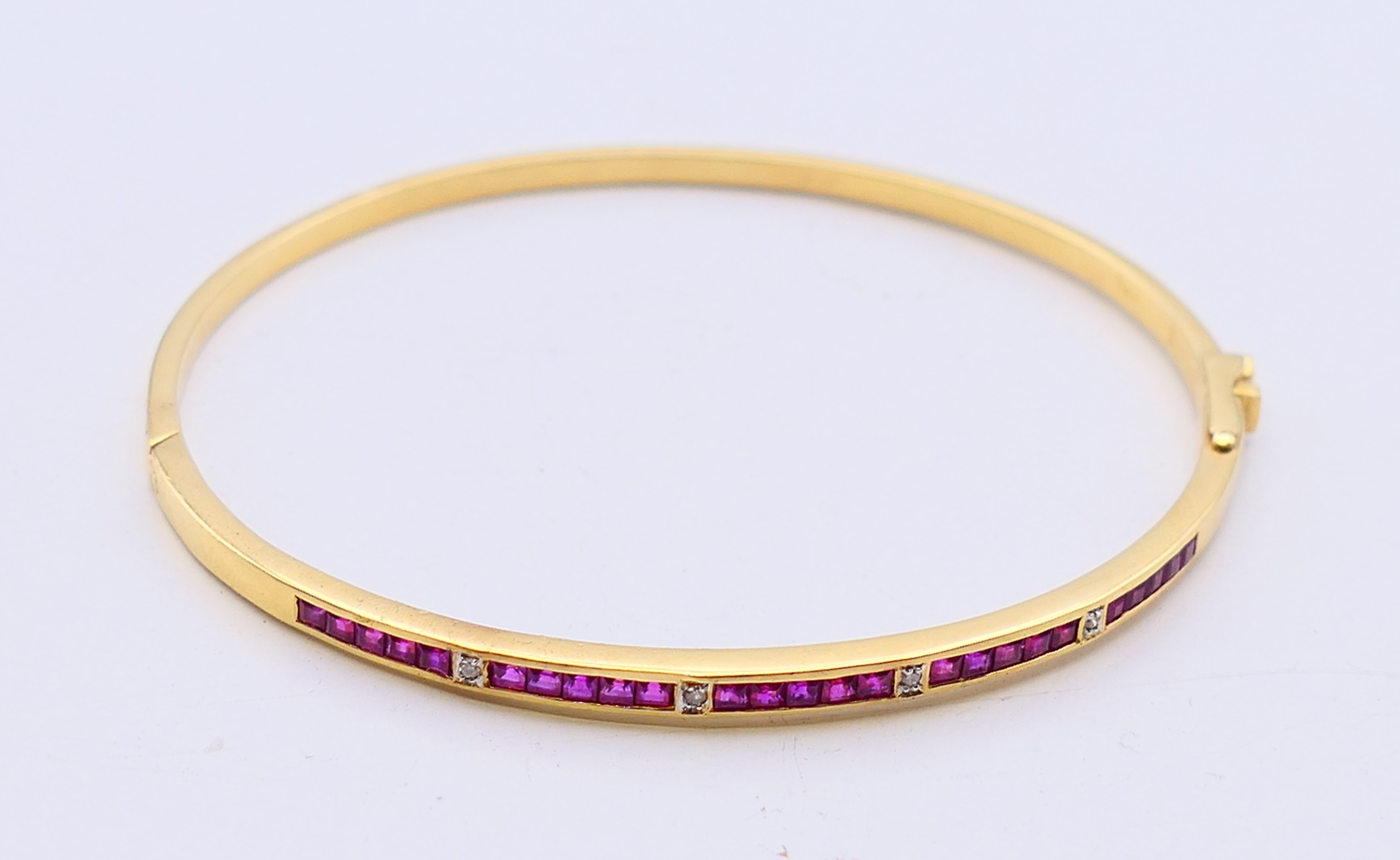 An 18 ct gold, ruby and diamond hinged bangle with twenty-five square shaped rubies (2mm),