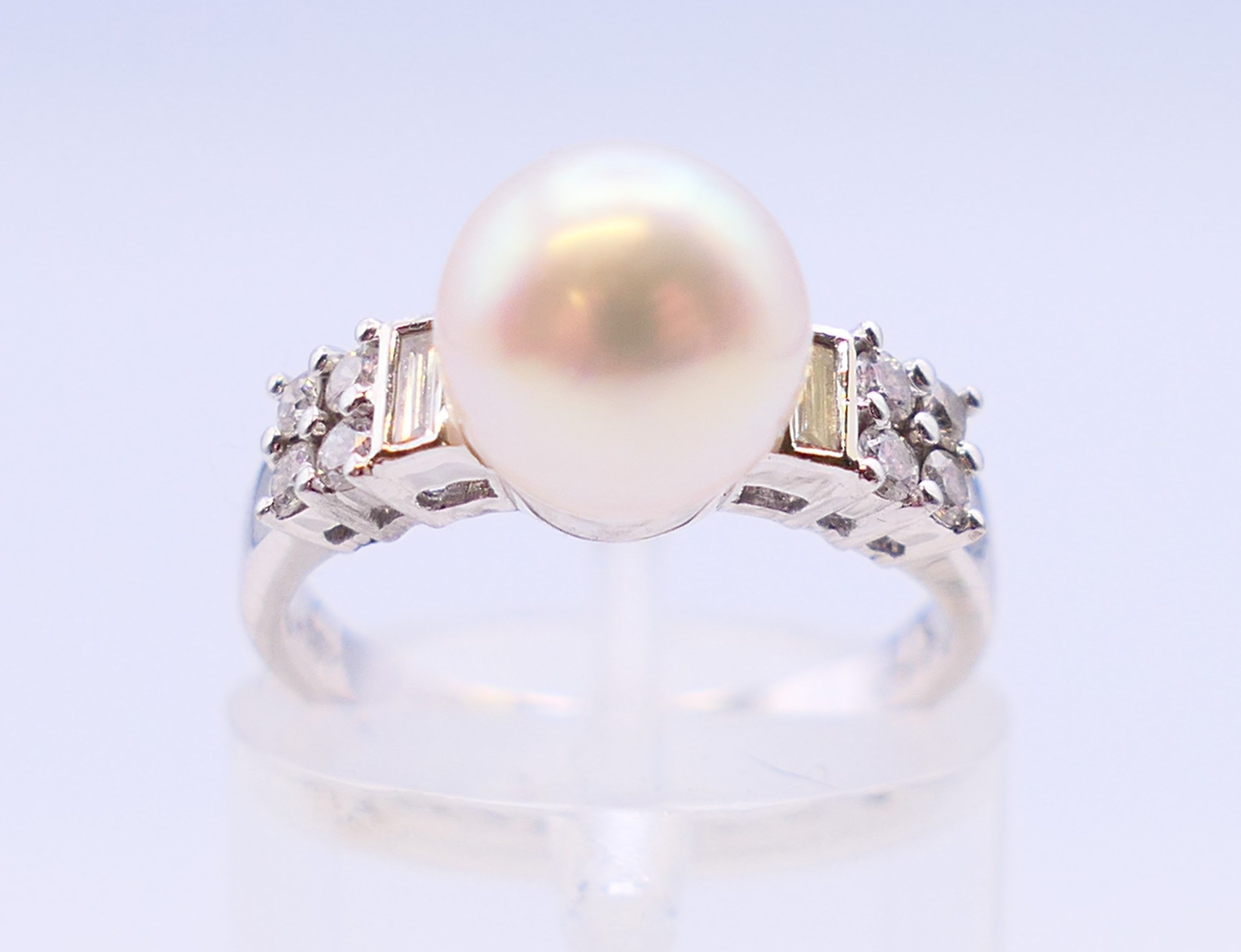 An 18 ct white gold and pearl ring flanked by baguette cut and round diamonds. Ring size I.