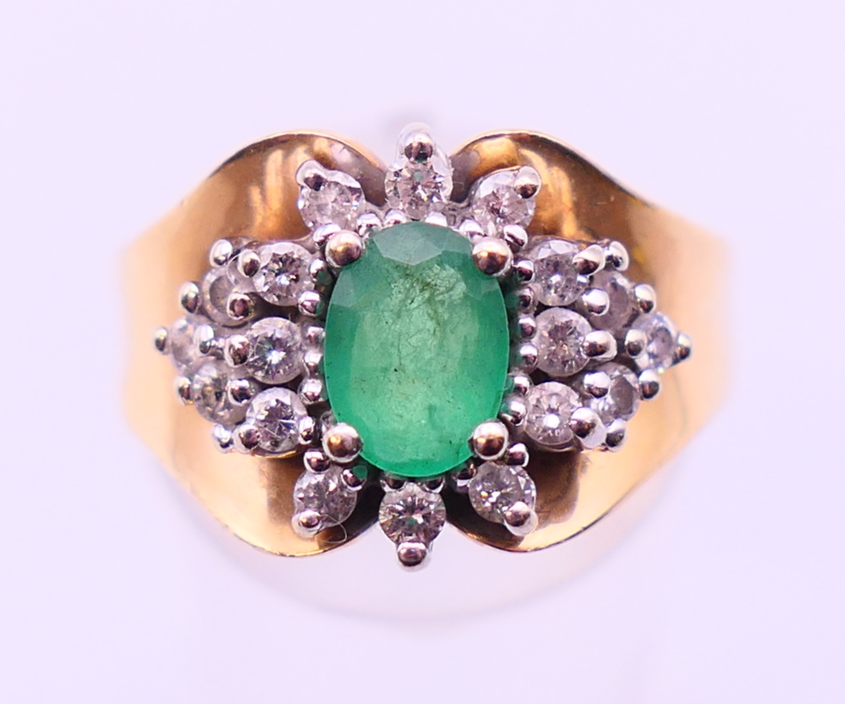A 14 ct gold, emerald and diamond cluster ring, the oval emerald (7.1 x 5.