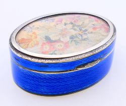 An oval blue enamel box with floral needlework inset lid. 184.4 grammes total weight. 8 cm wide.