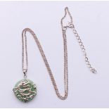 A silver dragon motif and jade pendant on a silver chain. Pendant 2 cm diameter, chain 44 cm long.