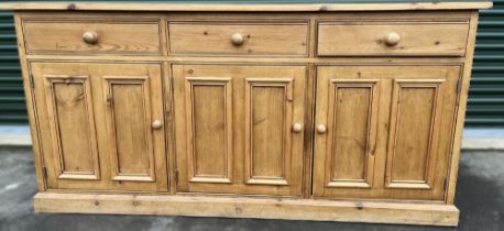 Waxed pine dresser base with three drawers above three twin panel doors with turned wooden handles