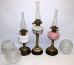 Three C19th century brass column oil lamps with black bases, incl. one with marbled pink glass