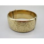 9ct yellow gold cuff hinged bangle, with half engraved foliage decoration, with safety chain,