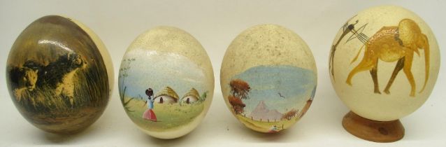 Four decorated ostrich eggs, one on turned wooden stand, 16cm