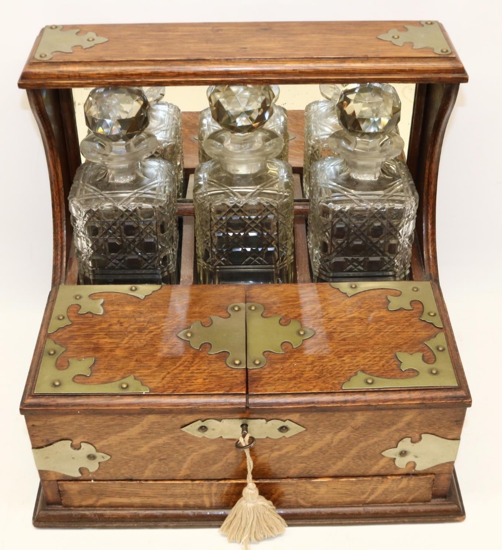 Late 19th century oak three bottle tantalus, metal mounts, twin lidded compartment, with key and