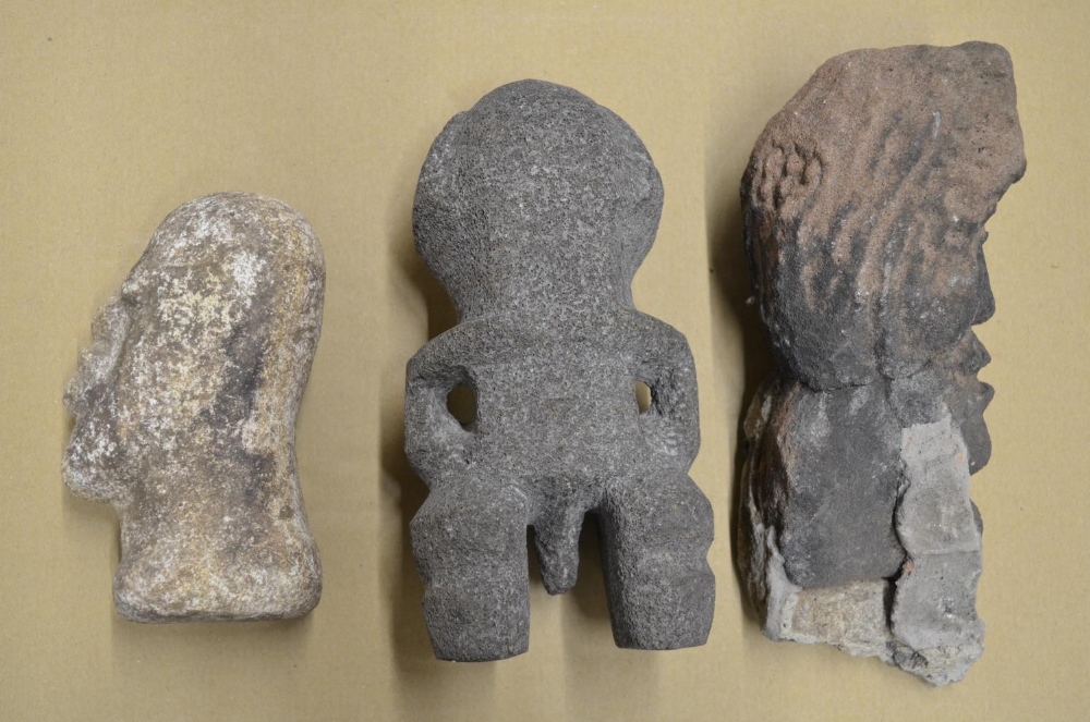 Three carved stone heads depicting an African man, an Aztec fertility symbol, other unknown with