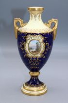 Coalport porcelain two handled urn, decorated with a lake scene vignette, within blue and gilt
