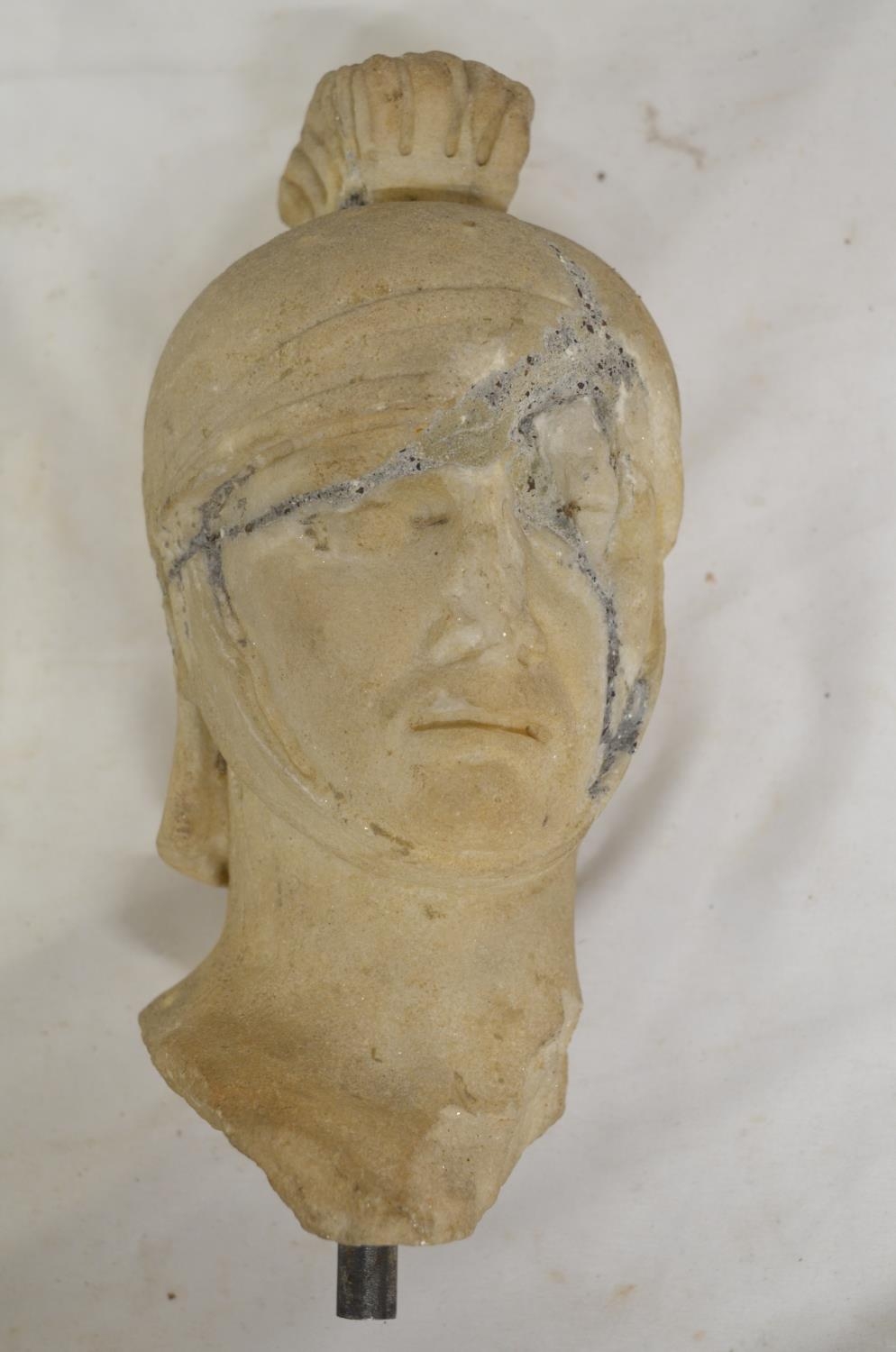 Carved marble head of a Roman soldier, damaged and pieced back together. With vertical stand rod, no