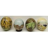 Four decorated ostrich eggs, one on turned wooden stand, 14cm.