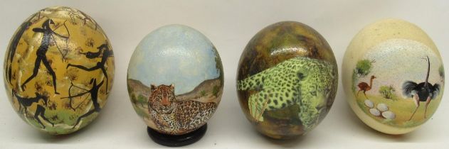 Four decorated ostrich eggs, one on turned wooden stand, 14cm.