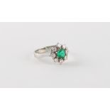 An 18ct white gold emerald & diamond cluster ring, claw set with a round cut emerald within a border