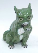 A Mosanic Pottery Green Glazed Model of a Cat, with green glass eyes, licking his bandaged paw, blue