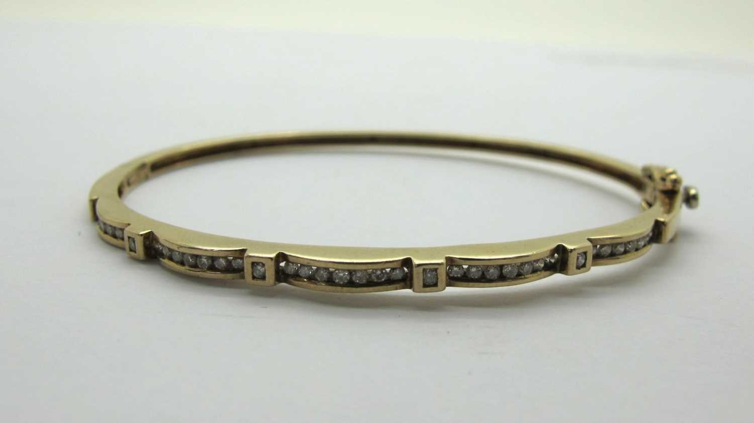 A Modern 9ct Gold Diamond Set Hinged Bangle, channel set with uniform stones, hinged to snap