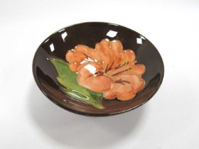A Moorcroft Dish, painted in the 'Hibiscus' Pattern in peach on a brown ground.